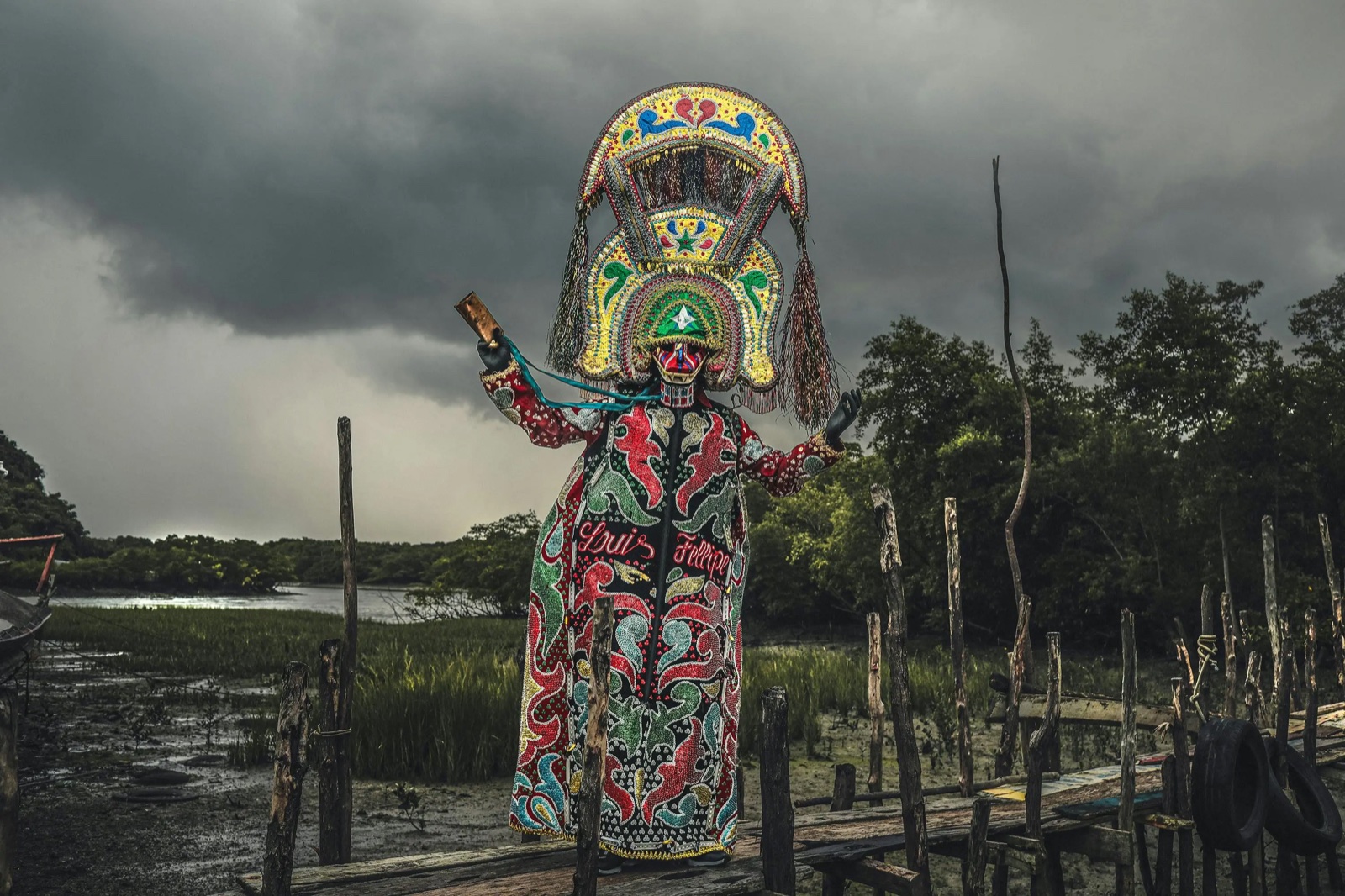 Márcio Vasconcelos — photographic work of an elaborately dressed masked figure in an estuarine landscape by Márcio Vasconcelos